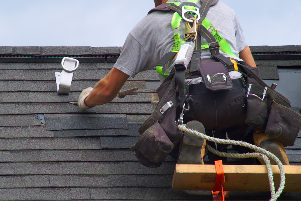 A handyman secured with rope works on repairing a roof